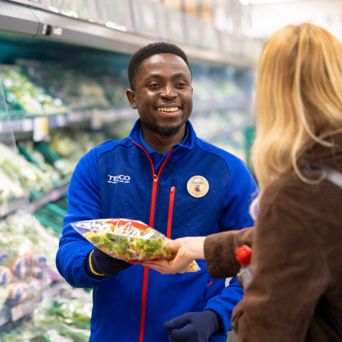 Photo of a Tesco employee handing customer a packet of vegetables