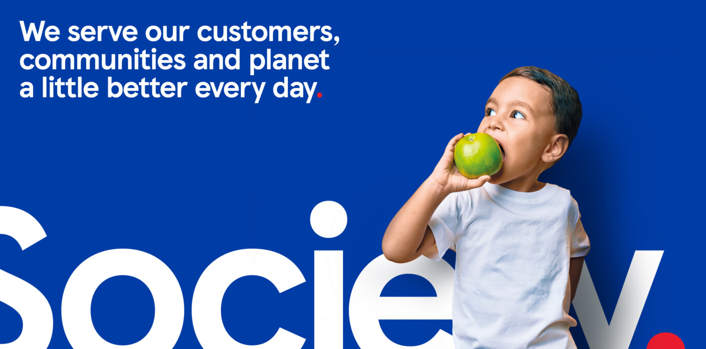 Child eating a green apple against a blue background with Tesco’s mission statement text